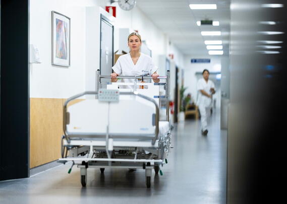 En sykepleier i uniform triller en sykeseng i en korridor.
