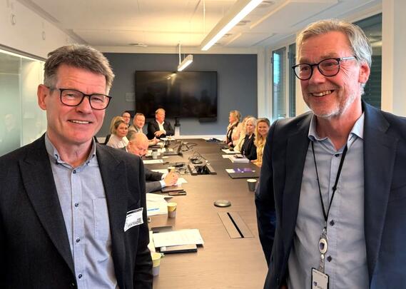 To menn med briller og dress smiler til kameraet.