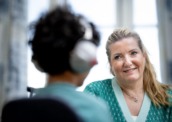 Dame med grønn genser som smiler til et barn med headset