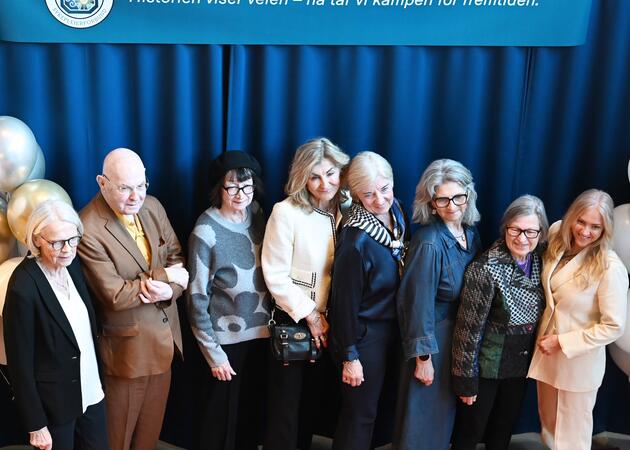 Åtte personer oppstilt foran et banner hvor det står "Historien viser veien - nå tar vi kampen for fremtiden."