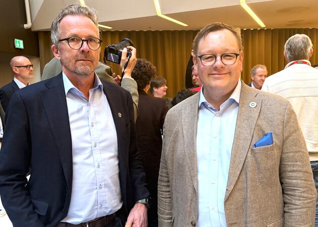 To menn med briller og dress står ved siden av hverandre