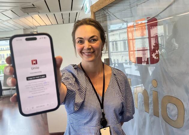 En smilende kvinne viser frem en mobilskjerm der man ser Unio-logoen.