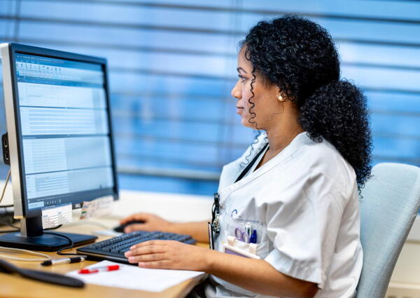 En sykepleier i uniform sitter og ser på en pc-skjerm.