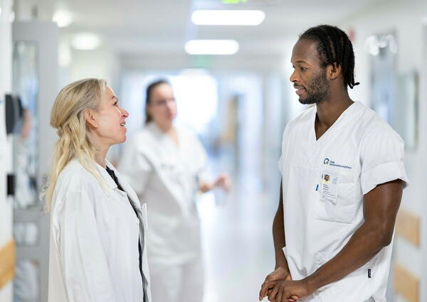 En mann og en dame i hvit sykepleieruniform snakker sammen i en korridor.