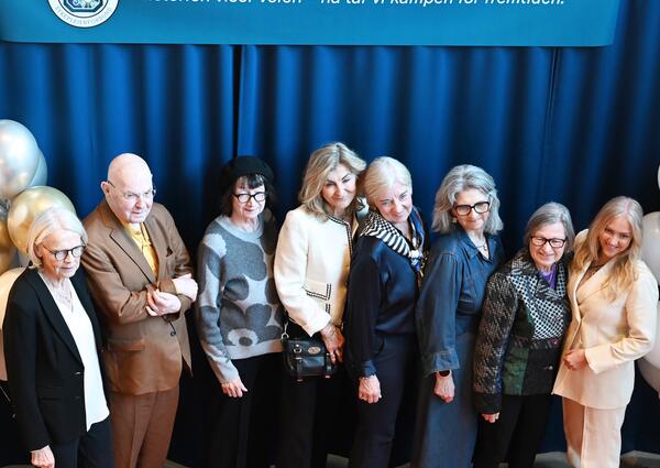Åtte personer oppstilt foran et banner hvor det står "Historien viser veien - nå tar vi kampen for fremtiden."