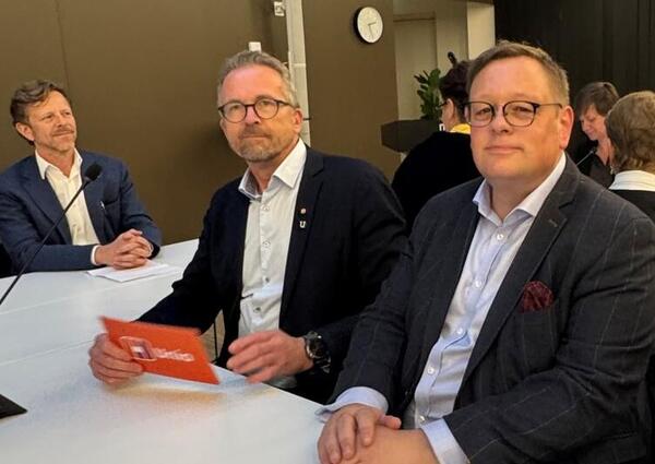 To menn i dress sitter ved siden av hverandre og ser mot fotografen.