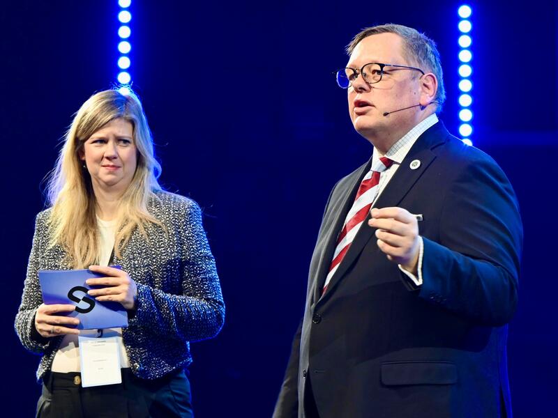 En kvinne og en mann står på en scene. Mannen prater til publikum.