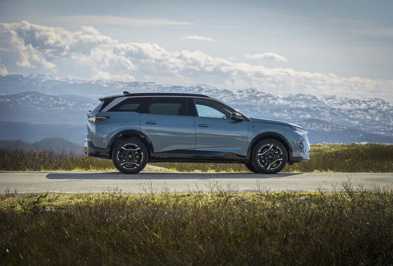 En bil sett fra siden, med snødekte fjell i bakgrunnen.