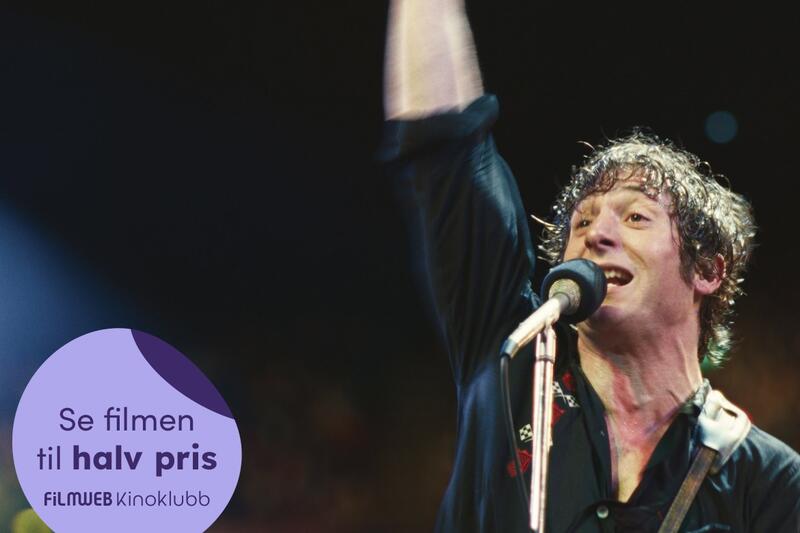 En musiker med gitar og den ene armen opp i våret synger inn i en mikron.