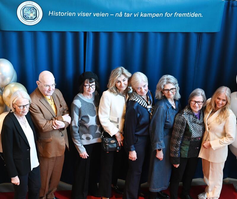 Åtte personer oppstilt foran et banner hvor det står "Historien viser veien - nå tar vi kampen for fremtiden."