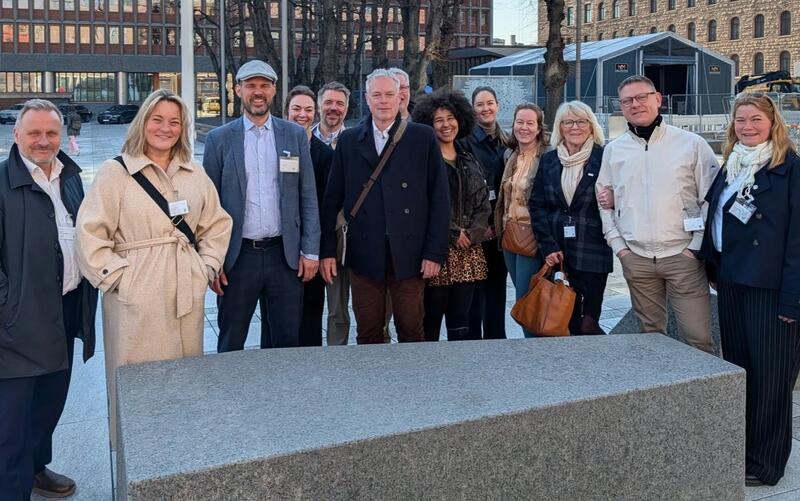 13 mennesker står oppstilt og smiler til kamera. Noen er delvis skjult bak andre.