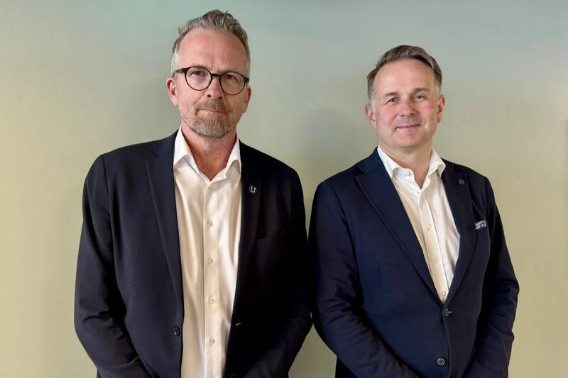 To menn i dress står ved siden av hverandre og ser mot fotografen.